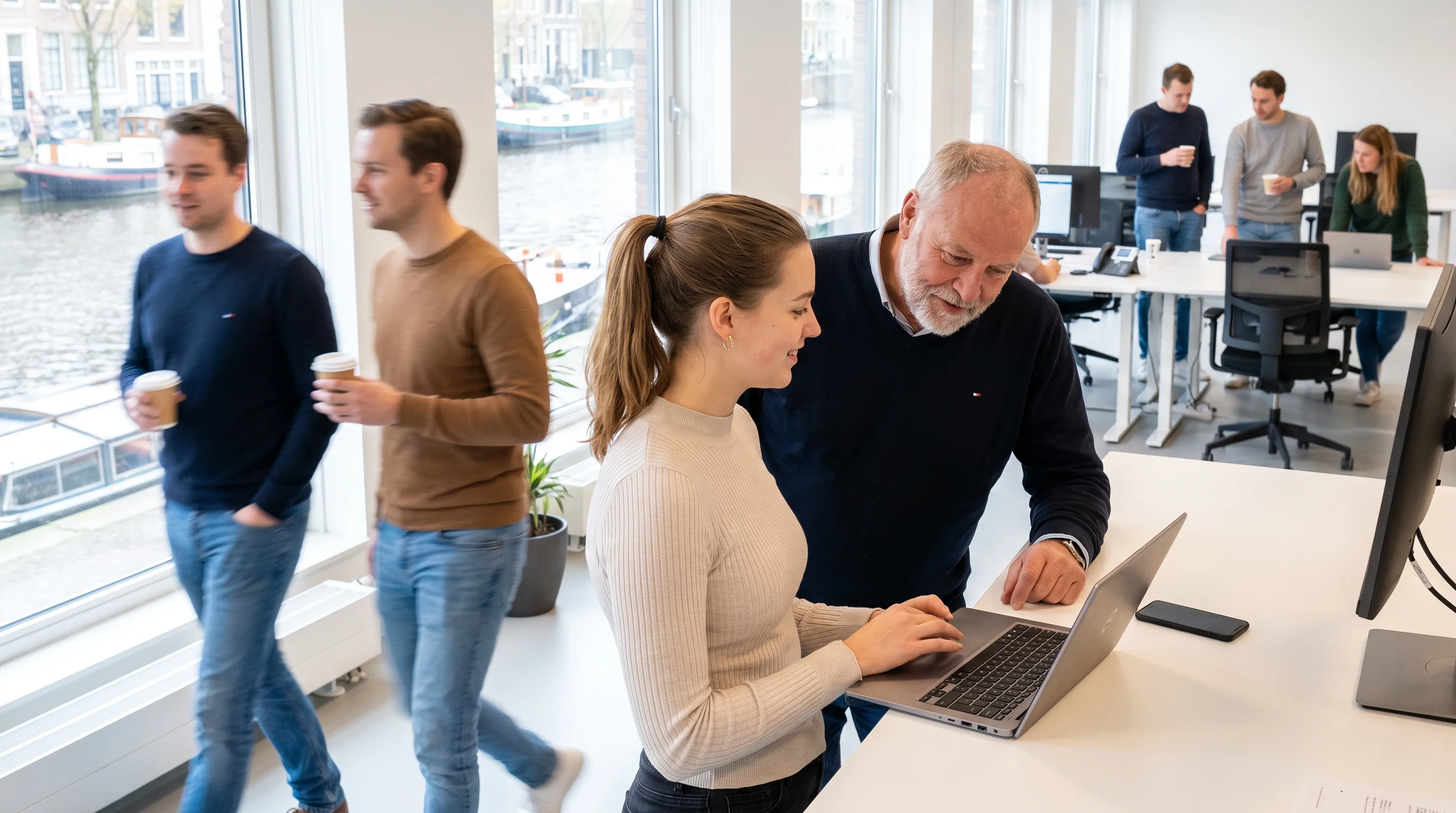 A developer shows a senior developer something on her laptop at a sunny software company